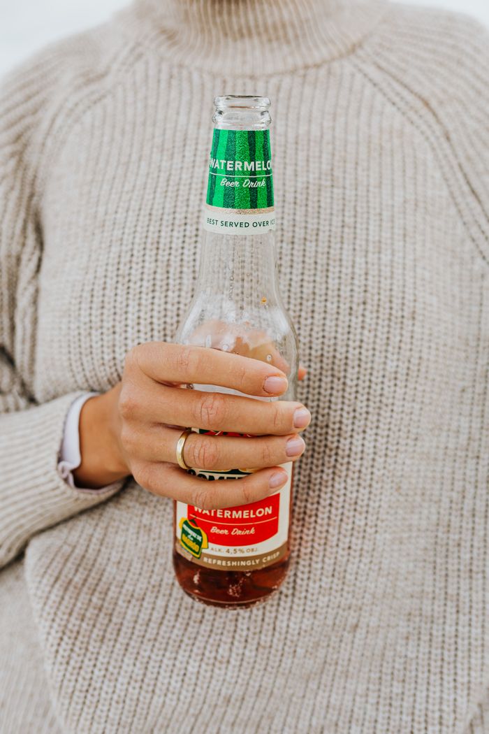 A person in a sweater holding a bottle of watermelon-flavored drink.