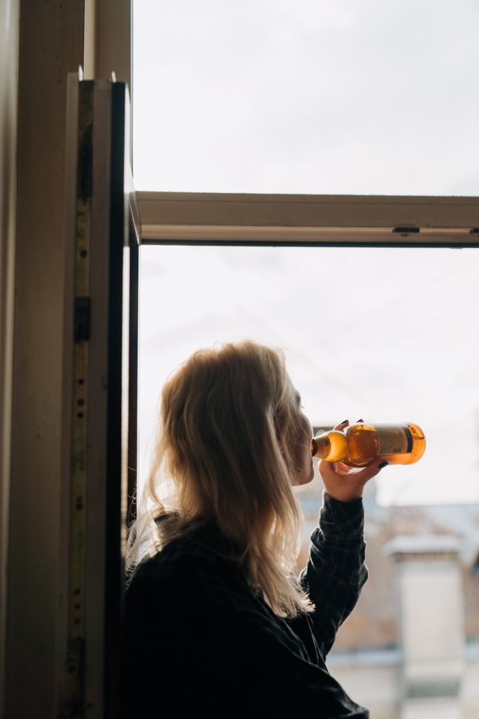 Silhouette of a woman enjoying a beer indoors by an open window.
