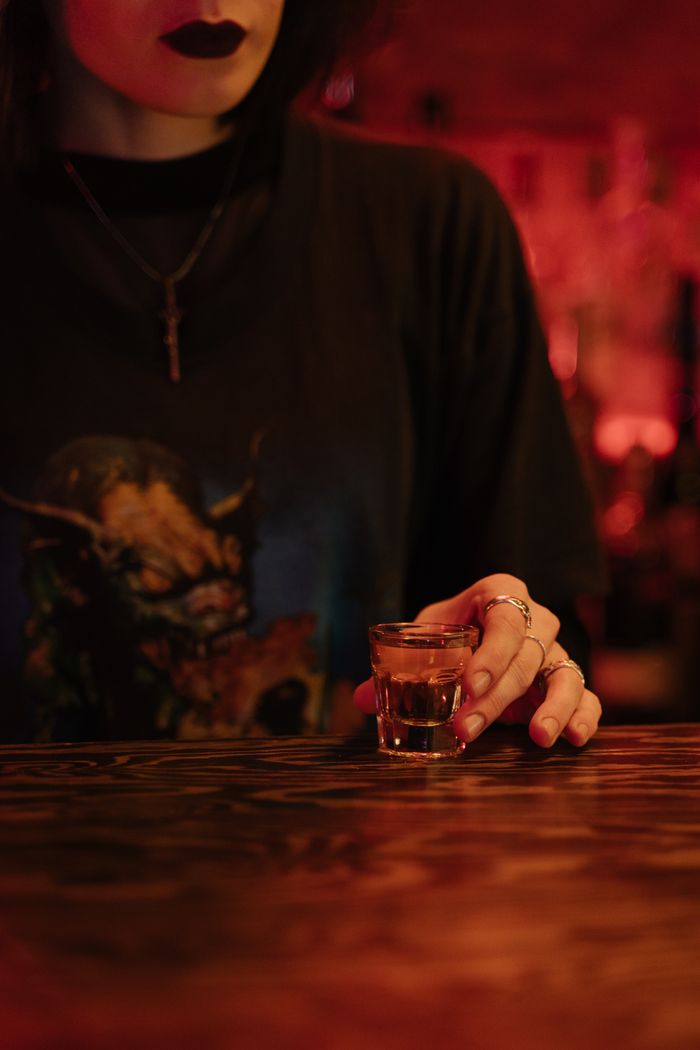 A person holding a shot glass in a moody bar ambience.